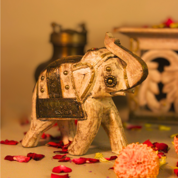 Decorative white wooden elephant with carved brass detailing placed amid festive flower petals