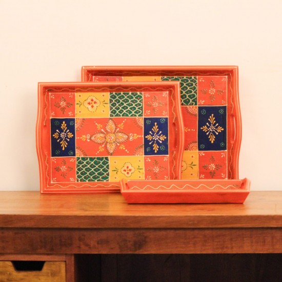 Hand Painted Orange Patchwork Tray – Large Large wooden serving tray in orange, hand painted in a colourful patchwork pattern of floral and geometric motifs in green, blue, and yellow, with cut-out side handles.