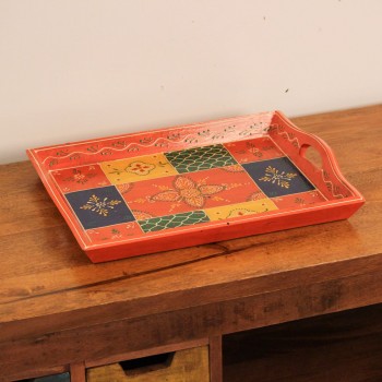 Large wooden serving tray in orange, hand painted in a colourful patchwork pattern of floral and geometric motifs in green, blue, and yellow, with cut-out side handles.