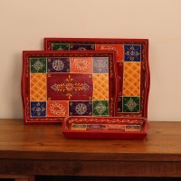 Hand Painted Red Patchwork Tray – Set of 3 Set of three nesting wooden serving trays in red, hand painted in a colourful patchwork pattern of floral and geometric motifs in green, blue, and yellow, with cut-out side handles.