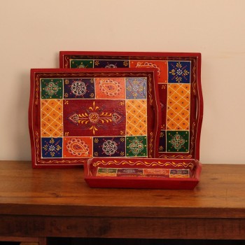 Hand Painted Red Patchwork Tray – Set of 3 Set of three nesting wooden serving trays in red, hand painted in a colourful patchwork pattern of floral and geometric motifs in green, blue, and yellow, with cut-out side handles.