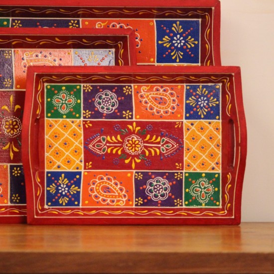 Hand Painted Red Patchwork Tray – Set of 3 Set of three nesting wooden serving trays in red, hand painted in a colourful patchwork pattern of floral and geometric motifs in green, blue, and yellow, with cut-out side handles.