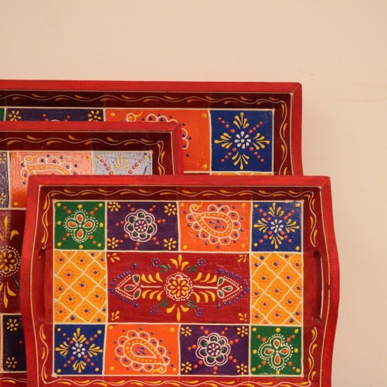 Hand Painted Red Patchwork Tray – Set of 3 Set of three nesting wooden serving trays in red, hand painted in a colourful patchwork pattern of floral and geometric motifs in green, blue, and yellow, with cut-out side handles.