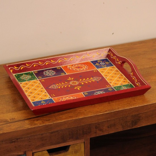 Hand Painted Red Patchwork Tray – Medium Medium wooden serving tray in red, hand painted in a colourful patchwork pattern of floral and geometric motifs in green, blue, and yellow, with cut-out side handles.