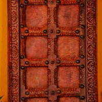 Handcrafted rustic red wooden door wall panel with intricate carvings and antique metal studs for traditional Indian wall decor