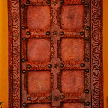 Handcrafted rustic red wooden door wall panel with intricate carvings and antique metal studs for traditional Indian wall decor