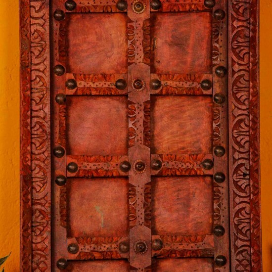 Handcrafted rustic red wooden door wall panel with intricate carvings and antique metal studs for traditional Indian wall decor