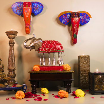 Hand-painted red Bell Elephant statuette with upraised trunk and ten metal bells on a wooden stand, styled with marigold garlands and a lit diya — traditional Rajasthani pooja décor (wood & metal).