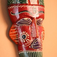 Hand Painted Tribal Face Mask – Red Hand-carved wooden tribal face mask hand painted in red with a green striped crown, purple diamond eyes, and detailed facial motifs in orange and white.