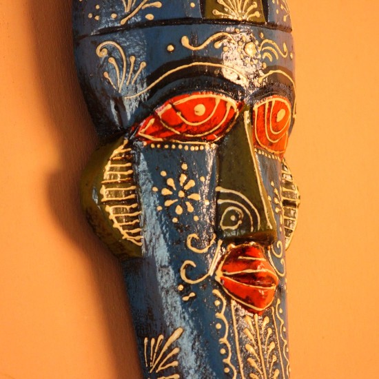 Hand-carved wooden tribal face mask hand painted in blue with a mustard-yellow crown, red eyes and lips, and fine white floral detailing across the face.