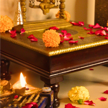 "Wooden square pooja chowki with brass embossing adorned with flowers and diya for festive decor