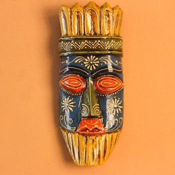 Hand-carved wooden tribal face mask hand painted in blue with red eyes and lips, a fringed mustard-yellow crown, a geometric zigzag forehead band, and white floral detailing across the face.