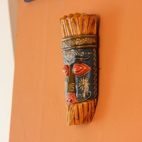Hand Painted Tribal Face Mask – Blue & Yellow Hand-carved wooden tribal face mask hand painted in blue with red eyes and lips, a fringed mustard-yellow crown, a geometric zigzag forehead band, and white floral detailing across the face.