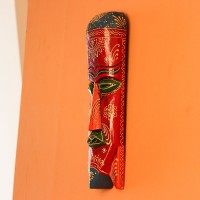 Hand Painted Tribal Face Mask – Maroon Mandala Hand-carved wooden tribal face mask in an elongated form, hand painted in maroon with a mandala-bordered crown, green eyes, and fine white floral detailing.
