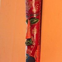 Hand Painted Tribal Face Mask – Maroon Mandala Hand-carved wooden tribal face mask in an elongated form, hand painted in maroon with a mandala-bordered crown, green eyes, and fine white floral detailing.