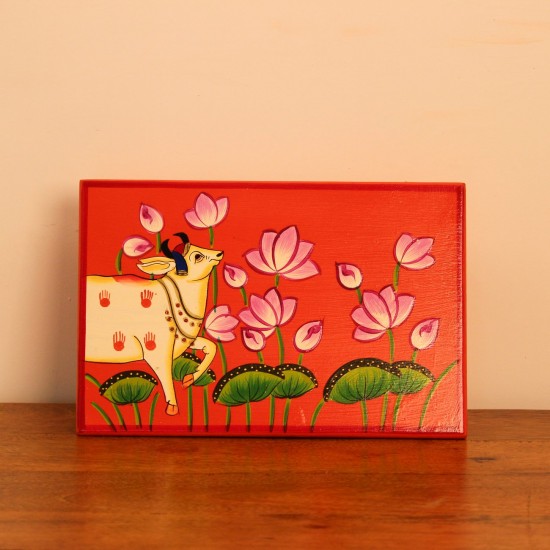 Hand Painted Cow & Lotus Chowki – Large Large wooden chowki hand painted in Pichwai style, featuring a cow standing amid blooming pink lotus flowers on a vivid red base, edged with a plain wooden border.