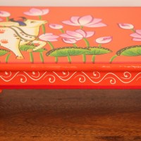 Hand Painted Cow & Lotus Chowki – Large Large wooden chowki hand painted in Pichwai style, featuring a cow standing amid blooming pink lotus flowers on a vivid red base, edged with a plain wooden border.