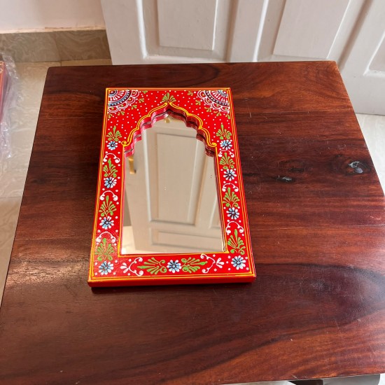 Hand-carved wooden mirror frame in a jharokha arch shape, hand painted in red with a fine floral border in blue, green, and white, framing an arched mirror at the centre.