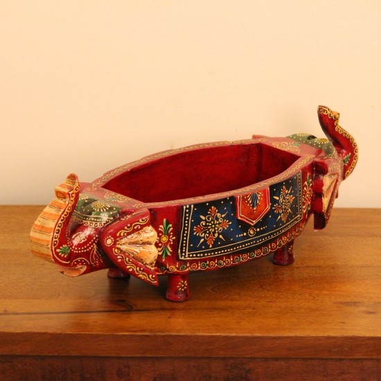Two Elephant Head Fruit Bowl – Hand Painted Red Wooden fruit bowl flanked by two carved elephant heads with brass tusk accents, hand painted in red with a blue floral panel across the bowl's front.
