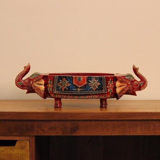 Two Elephant Head Fruit Bowl – Hand Painted Red Wooden fruit bowl flanked by two carved elephant heads with brass tusk accents, hand painted in red with a blue floral panel across the bowl's front.