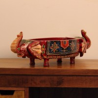 Two Elephant Head Fruit Bowl – Hand Painted Red Wooden fruit bowl flanked by two carved elephant heads with brass tusk accents, hand painted in red with a blue floral panel across the bowl's front.