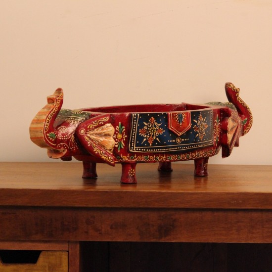 Two Elephant Head Fruit Bowl – Hand Painted Red Wooden fruit bowl flanked by two carved elephant heads with brass tusk accents, hand painted in red with a blue floral panel across the bowl's front.