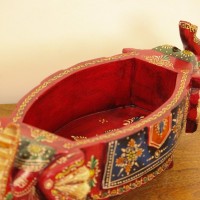 Two Elephant Head Fruit Bowl – Hand Painted Red Wooden fruit bowl flanked by two carved elephant heads with brass tusk accents, hand painted in red with a blue floral panel across the bowl's front.