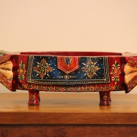 Two Elephant Head Fruit Bowl – Hand Painted Red Wooden fruit bowl flanked by two carved elephant heads with brass tusk accents, hand painted in red with a blue floral panel across the bowl's front.