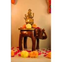 Decorative elephant brass art stool used as a pooja pedestal with an idol and flowers, adding traditional charm to a living space.