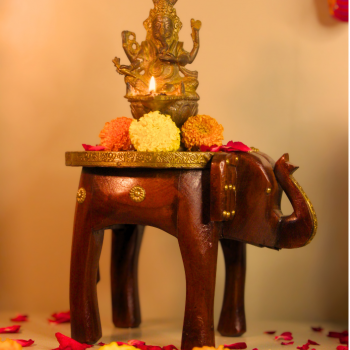 Decorative elephant brass art stool used as a pooja pedestal with an idol and flowers, adding traditional charm to a living space.