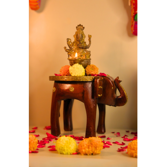 Decorative elephant brass art stool used as a pooja pedestal with an idol and flowers, adding traditional charm to a living space.