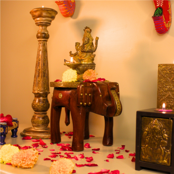 Decorative elephant brass art stool used as a pooja pedestal with an idol and flowers, adding traditional charm to a living space.