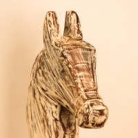 Hand-carved wooden horse head in a distressed whitewash finish, with a flowing textured mane, mounted on a slender black iron stand as a standalone decorative accent.