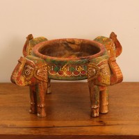 Hand Painted Wooden Elephant Bowl Stand Wooden bowl held up by three carved elephant heads, hand painted in red, yellow, and green with a floral mandala pattern inside the bowl and detailed motifs on the elephants.