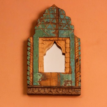 Front view of a hand-carved wooden mirror frame in a jharokha arch shape, in weathered green with chipped paint, a lattice-carved crown and an arched mirror at the centre.