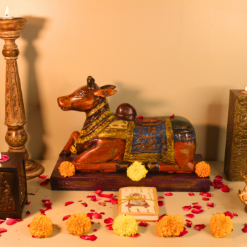 Handcrafted antique multicolor Nandi wooden sculpture surrounded by marigold flowers, candles, and rustic décor accents – traditional Indian handicraft from Udaipur.