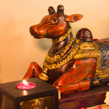 Handcrafted antique multicolor Nandi wooden sculpture surrounded by marigold flowers, candles, and rustic décor accents – traditional Indian handicraft from Udaipur.