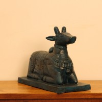 Dark teal blue carved wooden Nandi on a rectangular base placed on a wooden table as a pooja or console accent.