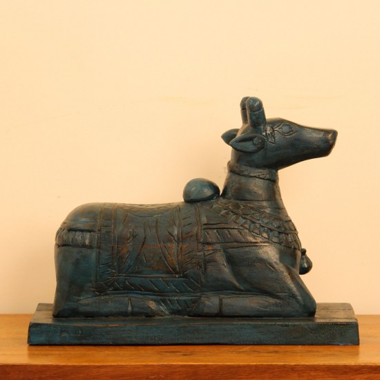 Dark teal blue carved wooden Nandi on a rectangular base placed on a wooden table as a pooja or console accent.