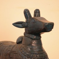 Dark teal blue carved wooden Nandi on a rectangular base placed on a wooden table as a pooja or console accent.