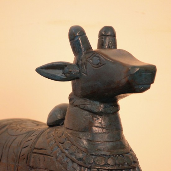 Dark teal blue carved wooden Nandi on a rectangular base placed on a wooden table as a pooja or console accent.