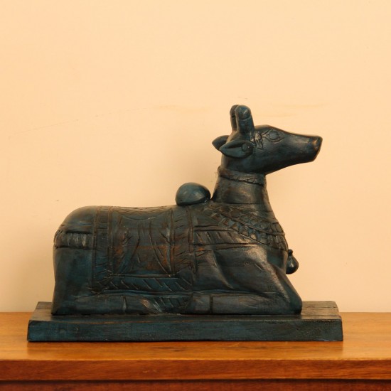 Dark teal blue carved wooden Nandi on a rectangular base placed on a wooden table as a pooja or console accent.