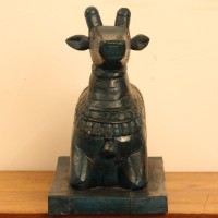 Dark teal blue carved wooden Nandi on a rectangular base placed on a wooden table as a pooja or console accent.