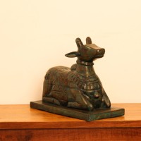 Teal green carved wooden Nandi on a rectangular base placed on a wooden table as a pooja or console accent.