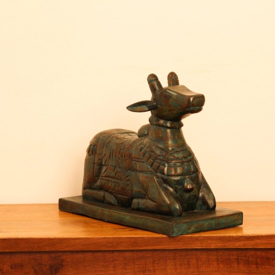 Teal green carved wooden Nandi on a rectangular base placed on a wooden table as a pooja or console accent.