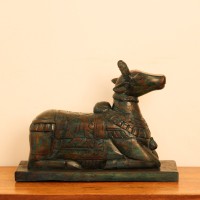 Teal green carved wooden Nandi on a rectangular base placed on a wooden table as a pooja or console accent.