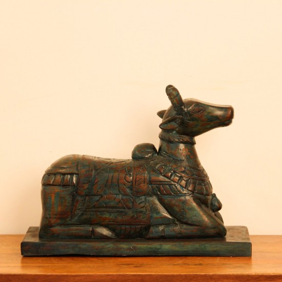Teal green carved wooden Nandi on a rectangular base placed on a wooden table as a pooja or console accent.