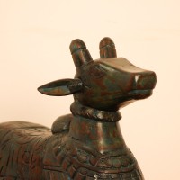 Teal green carved wooden Nandi on a rectangular base placed on a wooden table as a pooja or console accent.