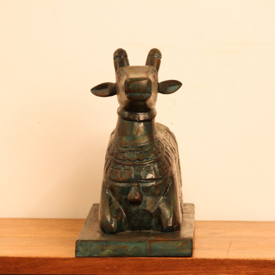 Teal green carved wooden Nandi on a rectangular base placed on a wooden table as a pooja or console accent.