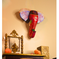 Hand-Painted Wooden Elephant Face Wall Decor in Red and Blue – Indune Red and blue hand-painted wooden elephant face wall hanging above Indian traditional setup